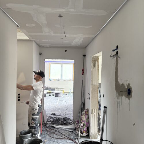 Ein Handwerker mit weißem Tshirt arbeitet konzentriert in einem renovierten Flur