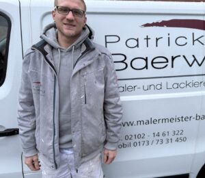 Ein lächelnder Mann in Arbeitskleidung steht vor einem weißen Handwerkerfahrzeug